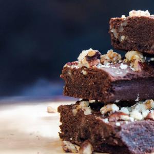 A stack of chocolate and pecan brownies, sprinkled with pecan crumbs and crushed walnut, fresh out of the oven